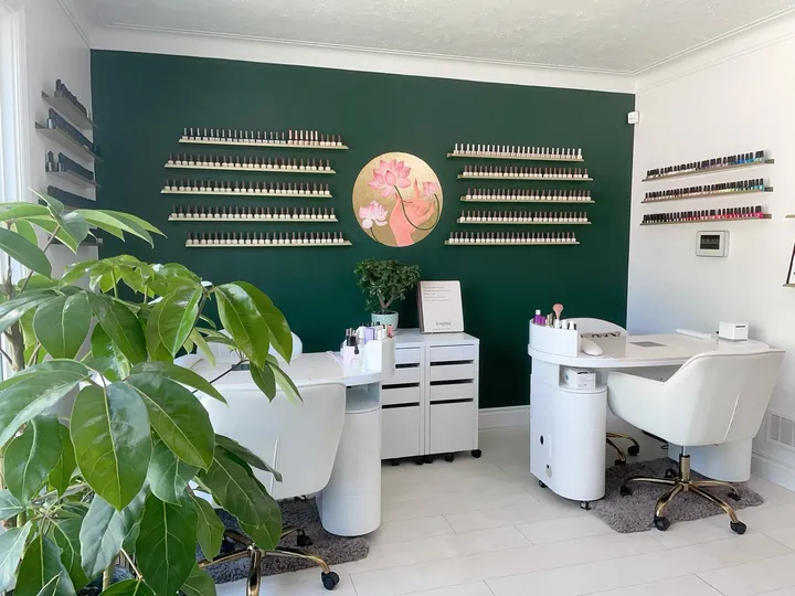 The bright nail room with white chairs and nail desks, a large plant and the lotus painting on the green wall